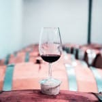 A glass of red wine elegantly placed on a wooden barrel in a Stellenbosch winery cellar.